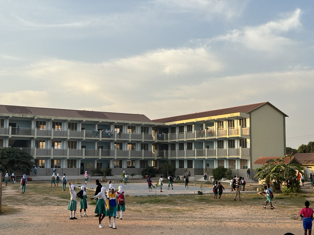 A three-storey cream school building with a playground in the front and school children milling.